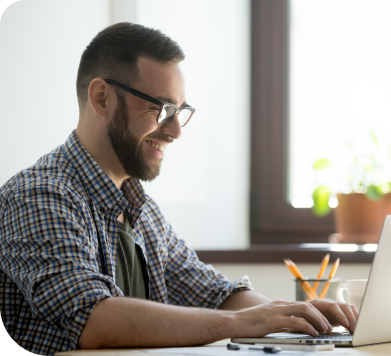 A smiling man using a laptop in an office environment.