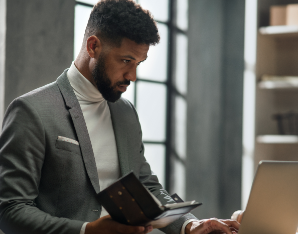 A man in a gray suit compares his notes with what his computer is displaying.